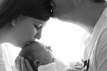 Eltern küssen sich mit nugeborenem Baby auf dem Arm